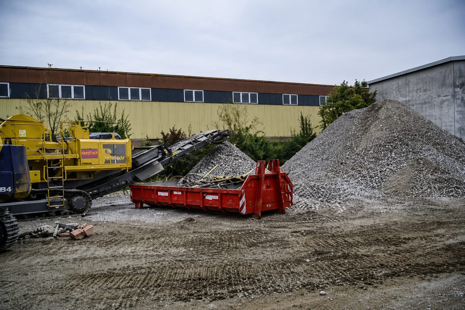 Mobile Brecheranlage neben Schotterhaufen auf einem Recyclinghof